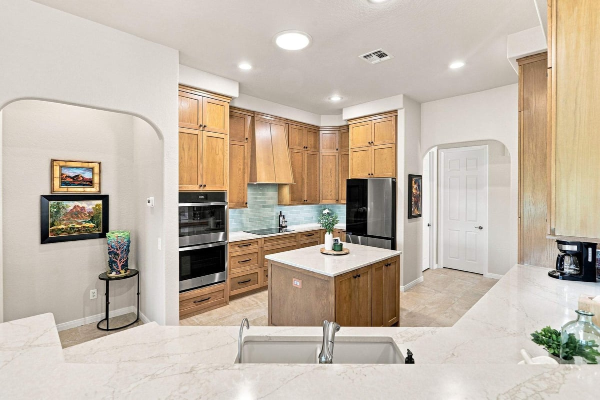 Wide view of Roseheart kitchen with natural wood cabinetry, blue-green tile backsplash, and center island.