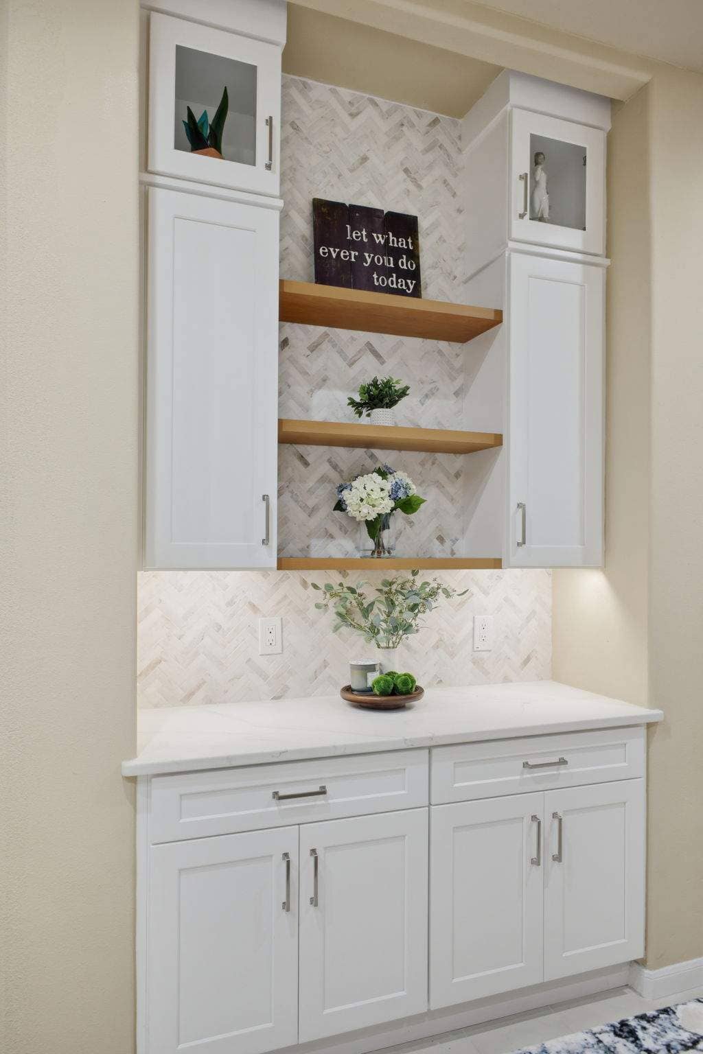 Built-in kitchen hutch with white cabinets, wood floating shelves, and herringbone tile in Deerfield, San Antonio. Built-in kitchen hutch with white cabinets, wood floating shelves, and herringbone tile in Deerfield, San Antonio.