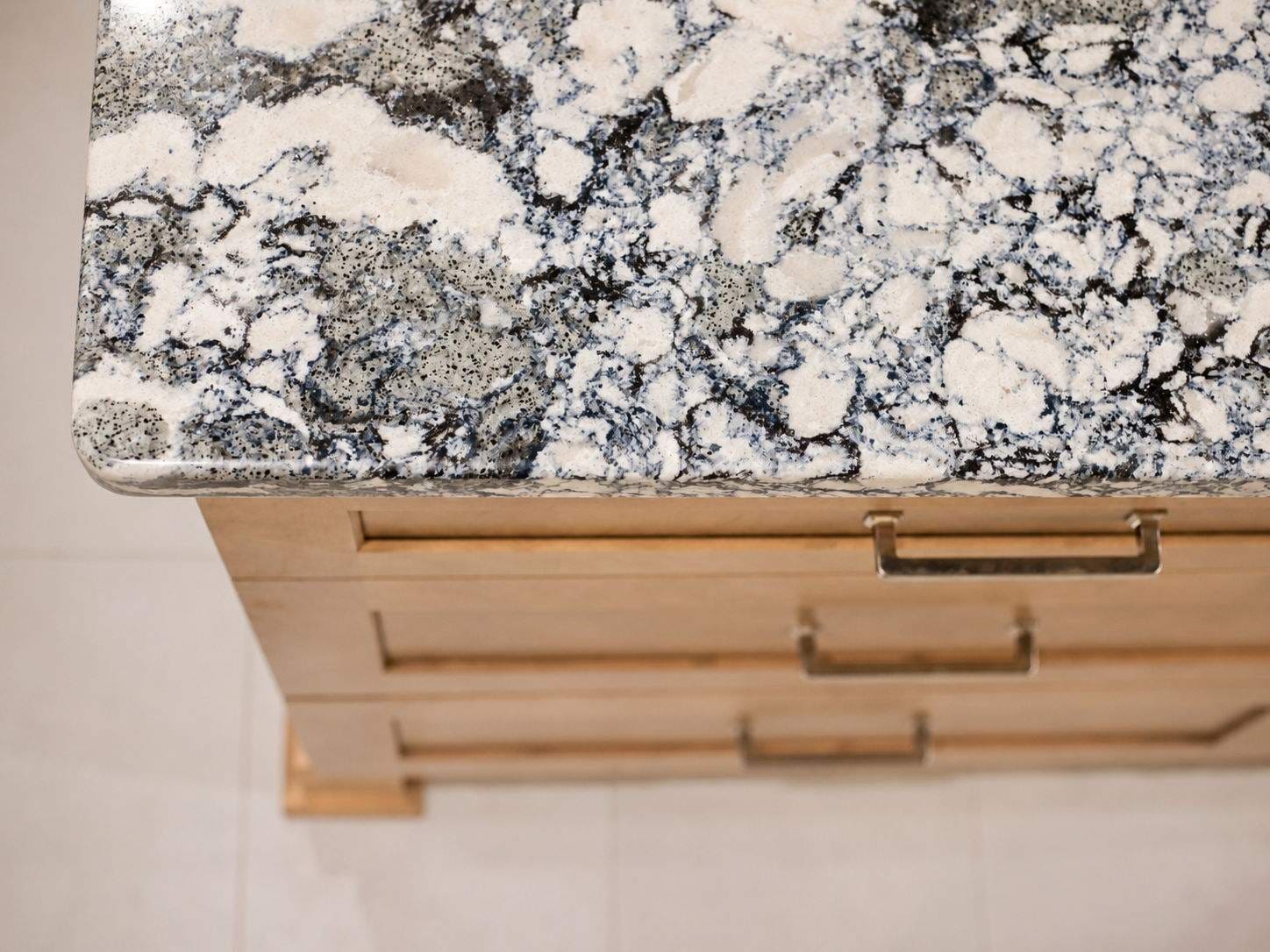 Close-up of a blue, white, and gray patterned stone island countertop above natural wood drawers.
