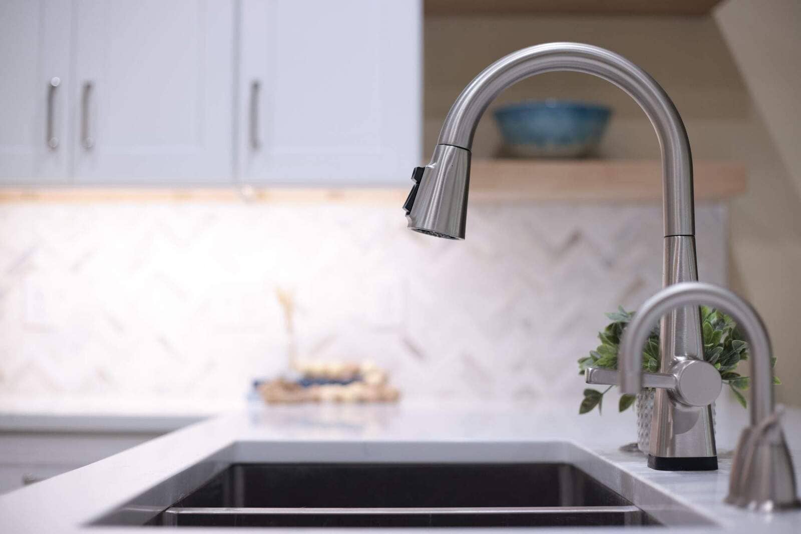 Close-up of a brushed nickel pull-down faucet and stainless sink in a bright remodeled kitchen.