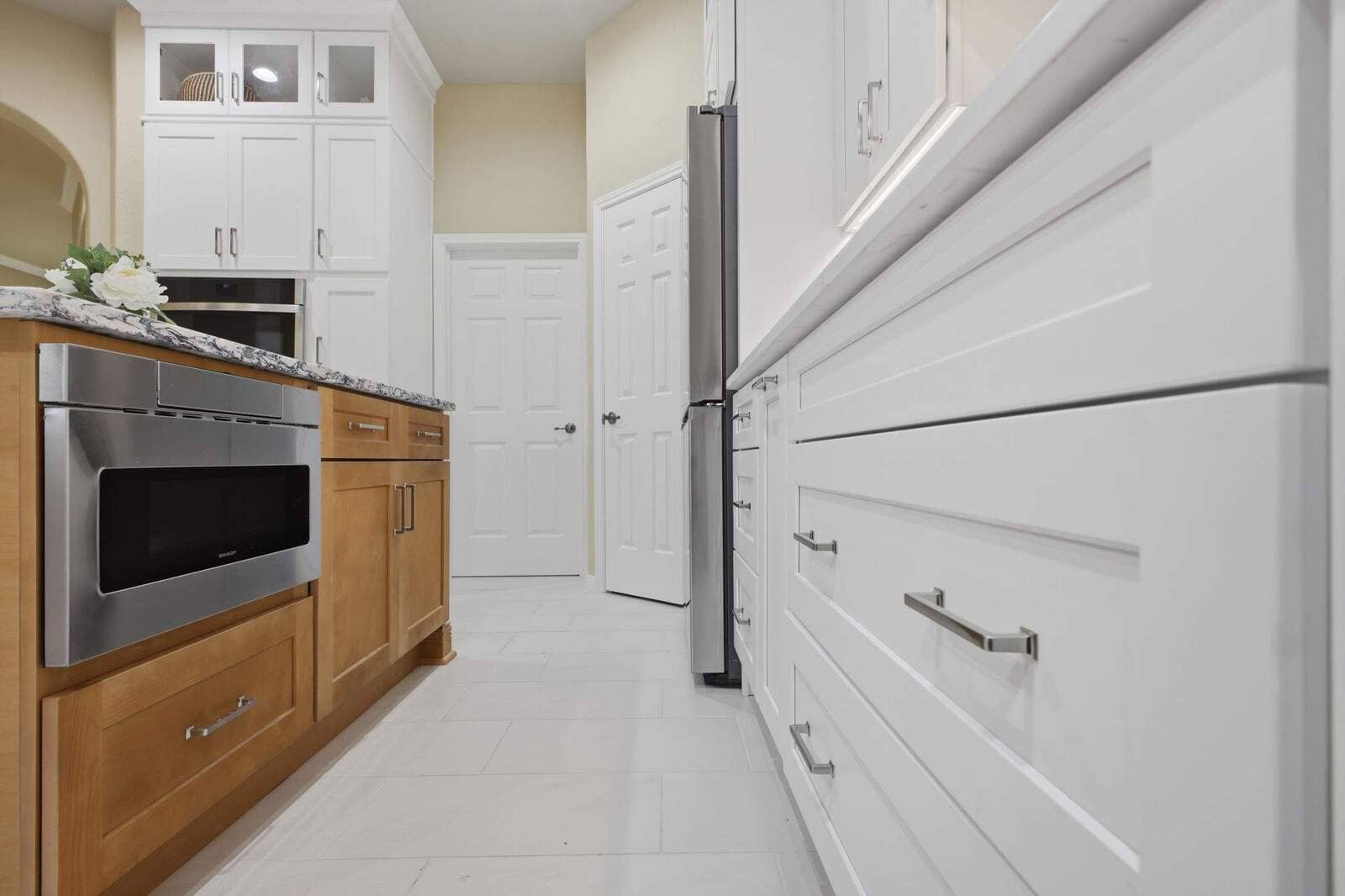 Low-angle view of white drawers, wood cabinetry, stainless appliances, and light tile flooring in a remodeled kitchen.