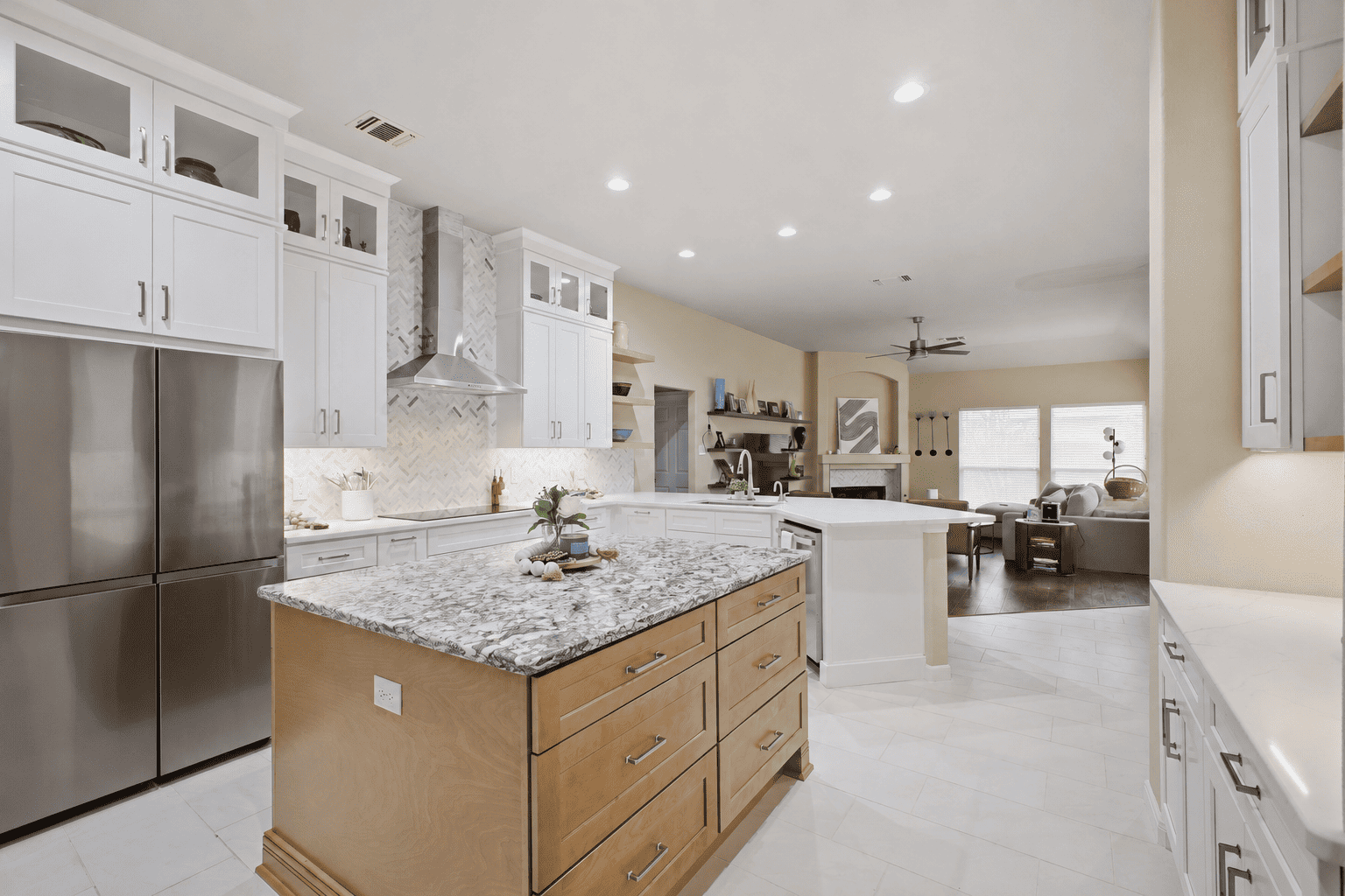 Open San Antonio kitchen with white cabinetry, patterned stone island, stainless appliances, and living room views.