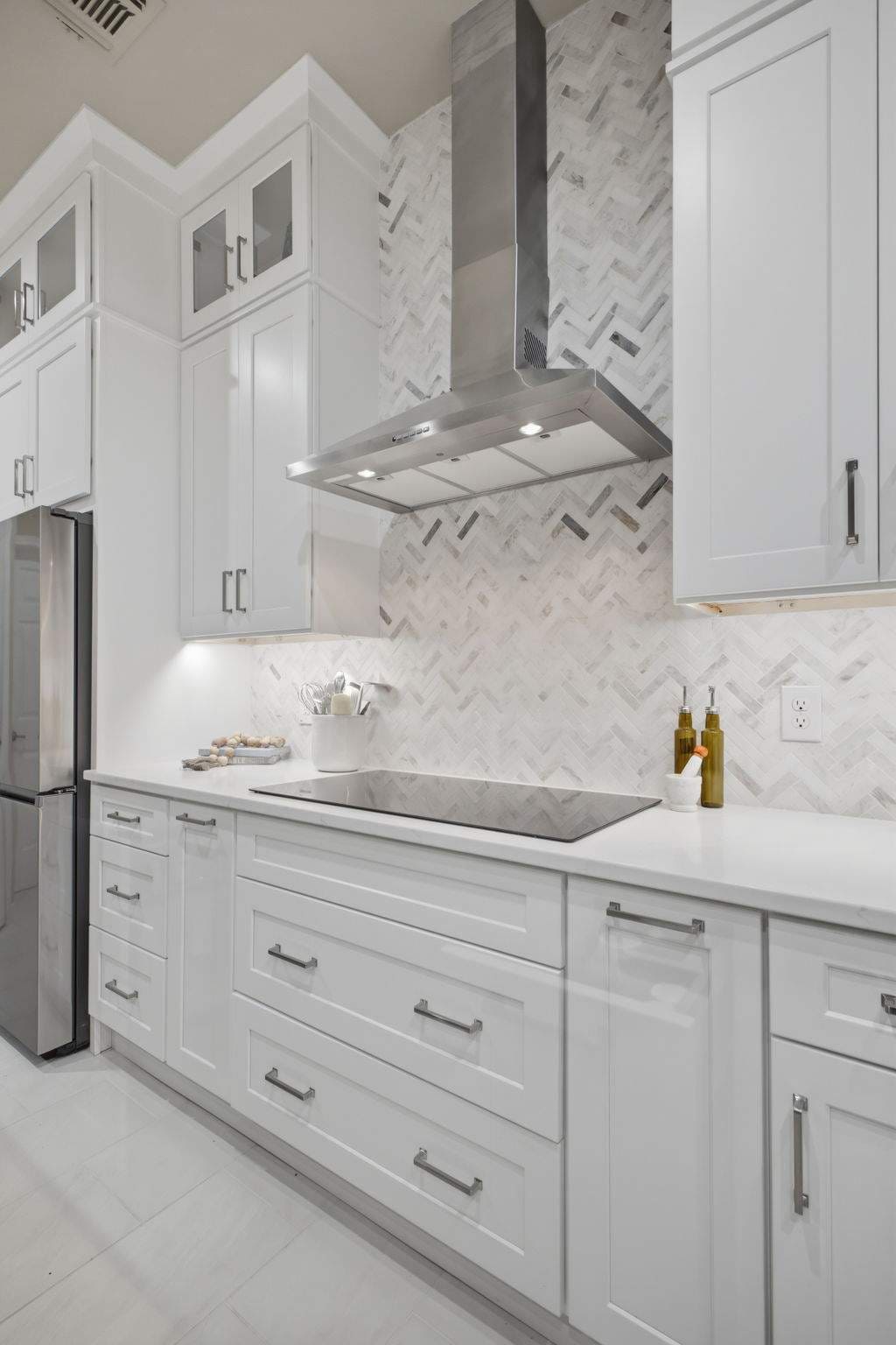 White kitchen cabinets, stainless range hood, and herringbone backsplash in a bright Deerfield remodel.