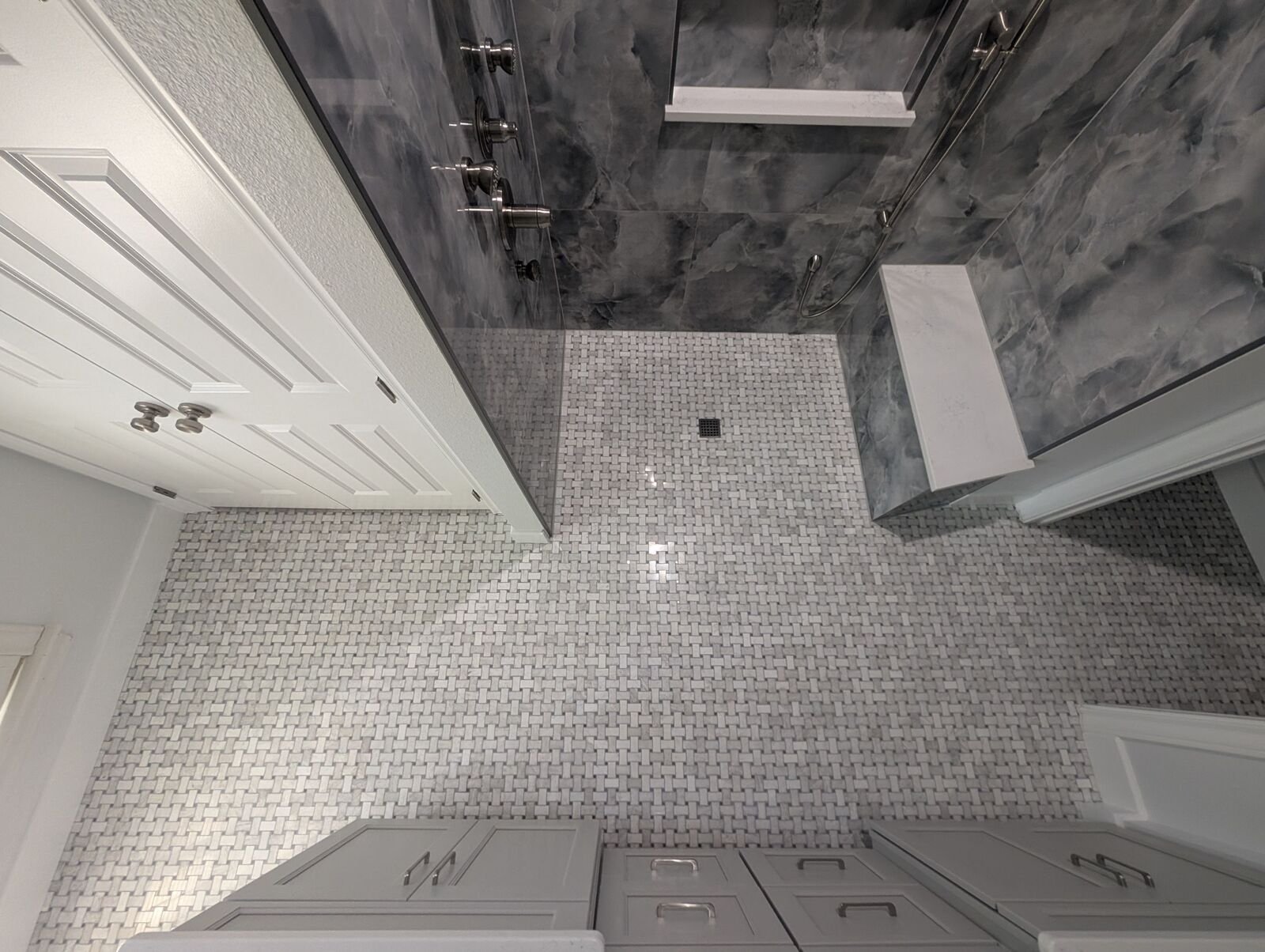 Remodeled bathroom floor with gray mosaic tile, glass shower entry, white doors and gray cabinetry.