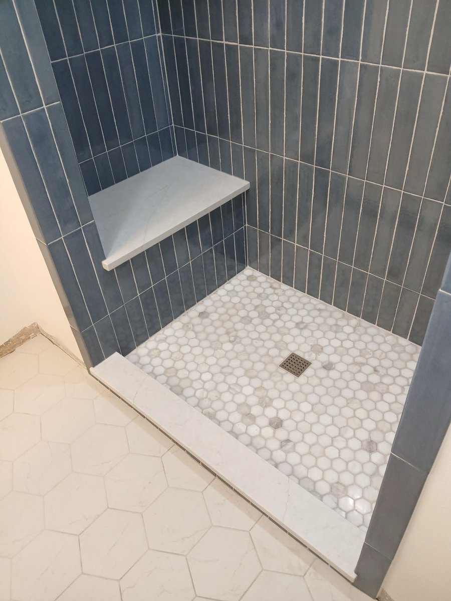 Walk-in shower with vertical blue tile, built-in bench, and marble hex floor
