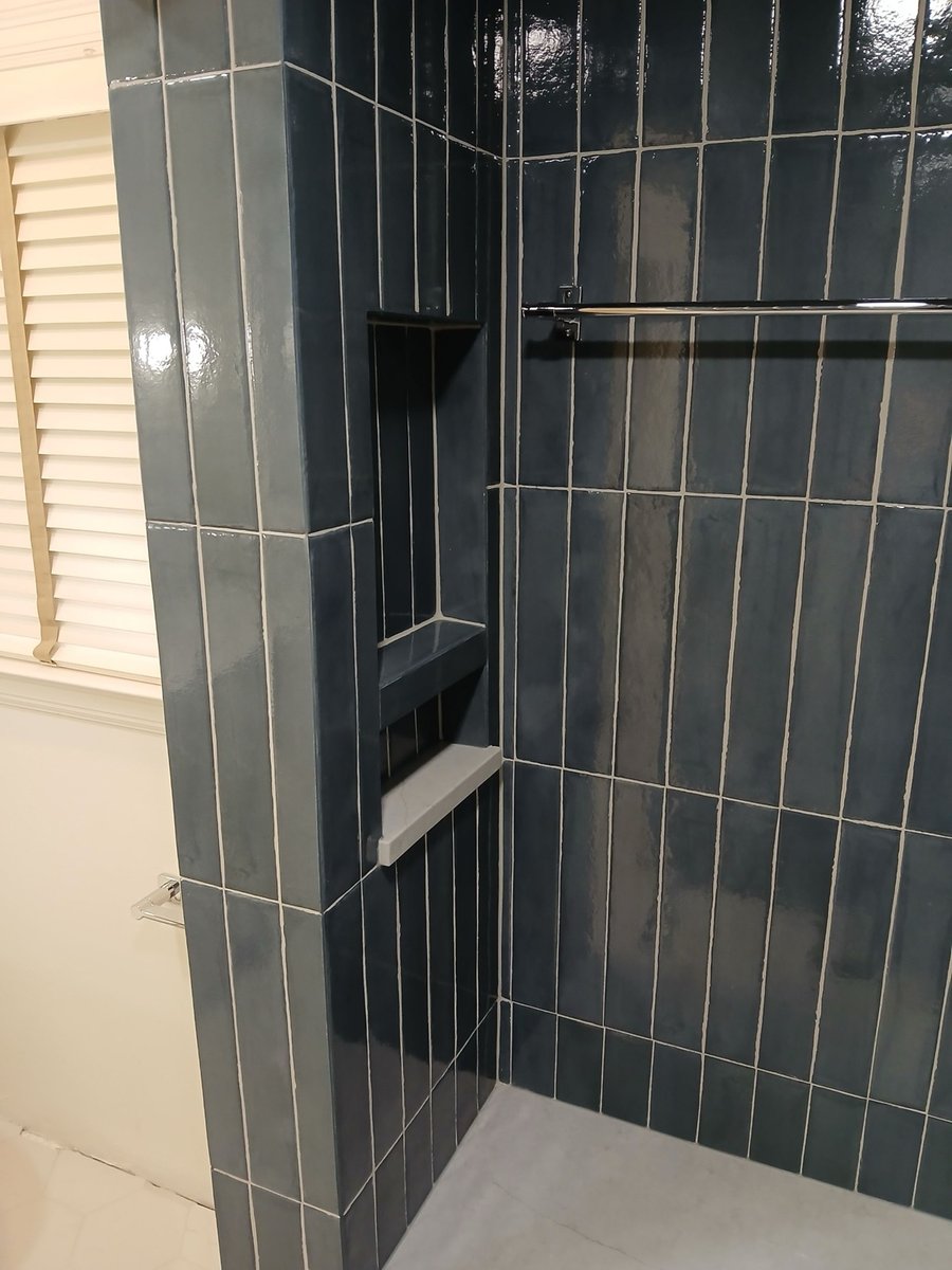 Glossy navy stacked tile shower wall with recessed niche and chrome bar