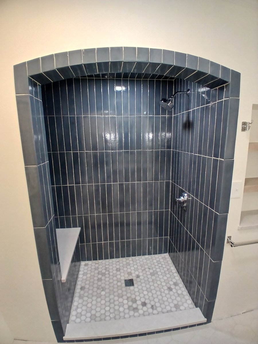 Arched walk-in shower with navy vertical tile, rainfall head, and marble hex floor