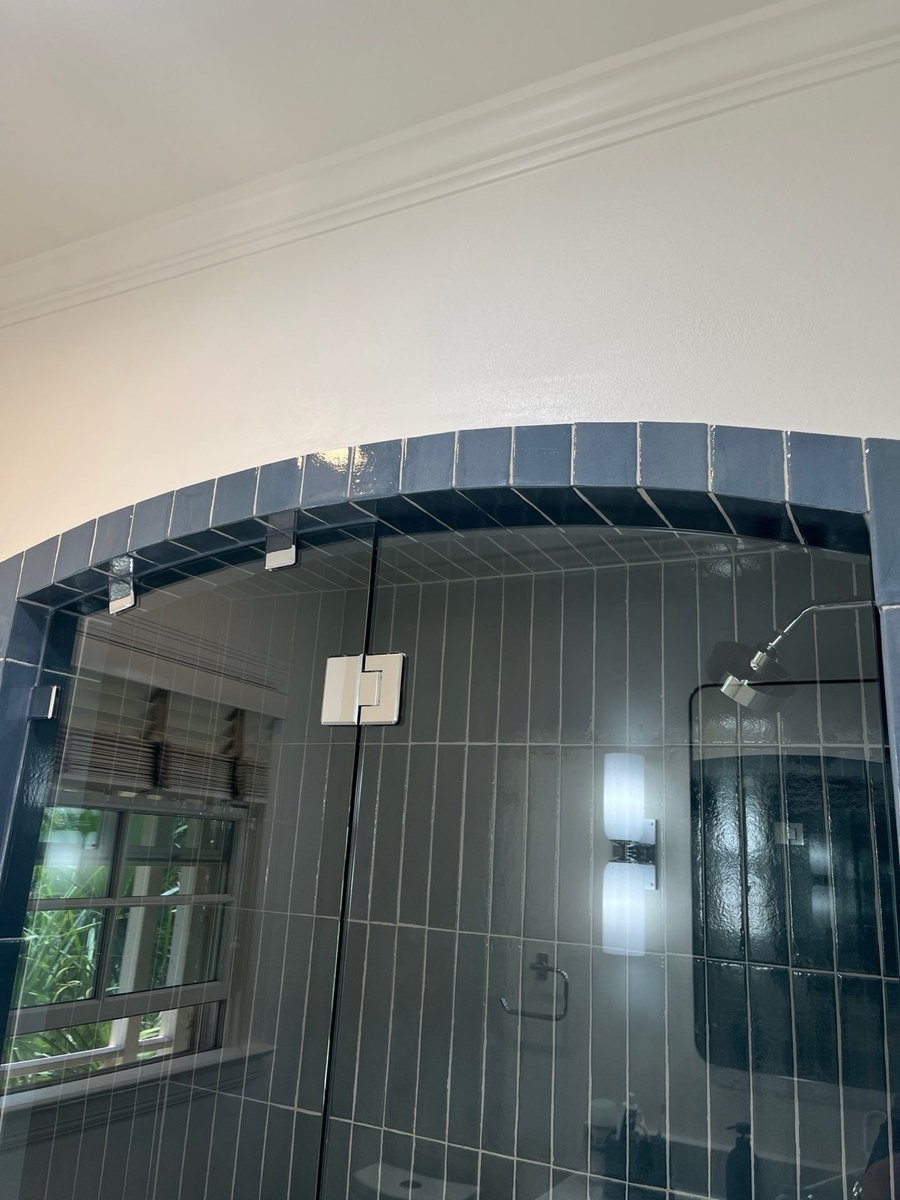 Top of arched glass shower with navy tile, chrome sconce, and window