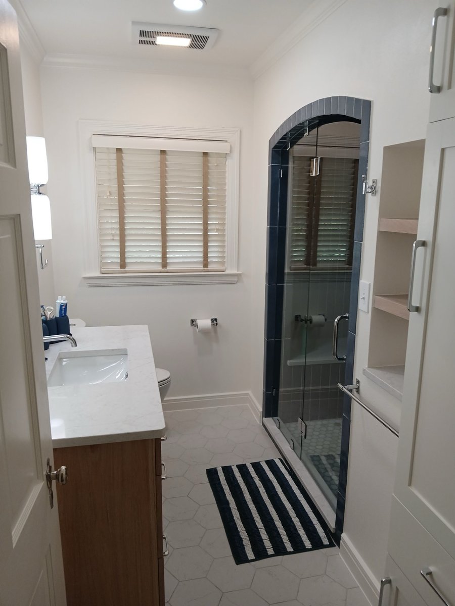 Narrow bath with wood vanity, white marble counter, and arched navy tile shower