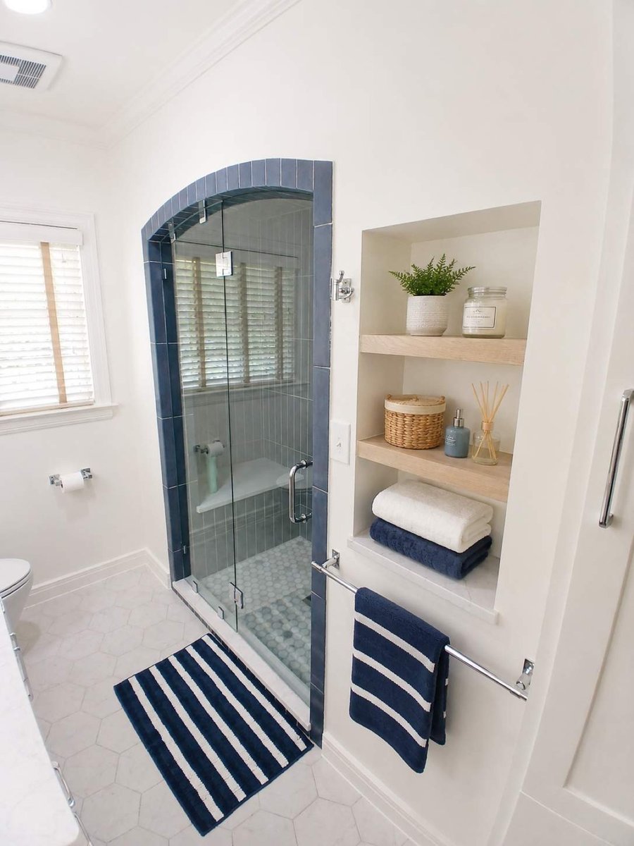 Arched navy shower beside built-in niche shelves with towels and decor