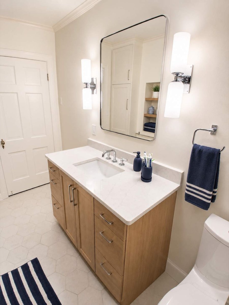 Wood vanity with white quartz top, framed mirror, sconces, and navy towel