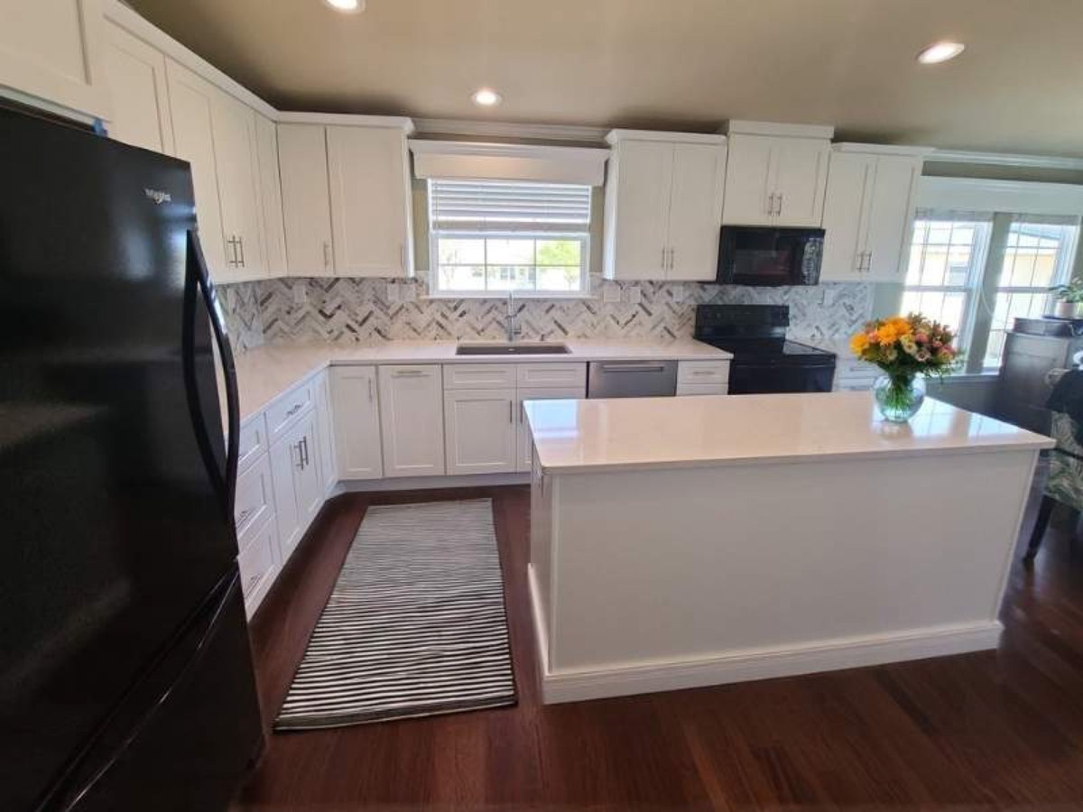 White kitchen with herringbone marble backsplash, black appliances and island