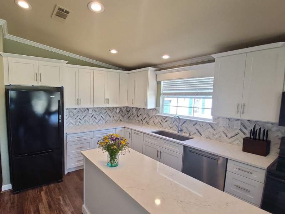 L-shaped white kitchen with vaulted ceiling, marble counters and island