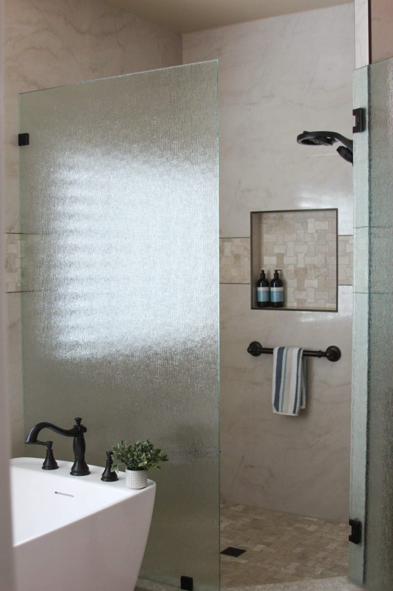 Rain-glass shower partition beside marble wall with niche and bronze fixtures