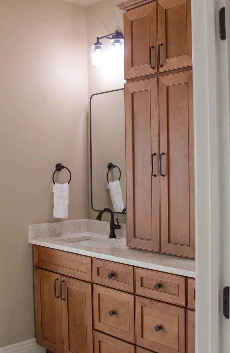Maple vanity and tall linen tower with framed mirror and bronze faucet