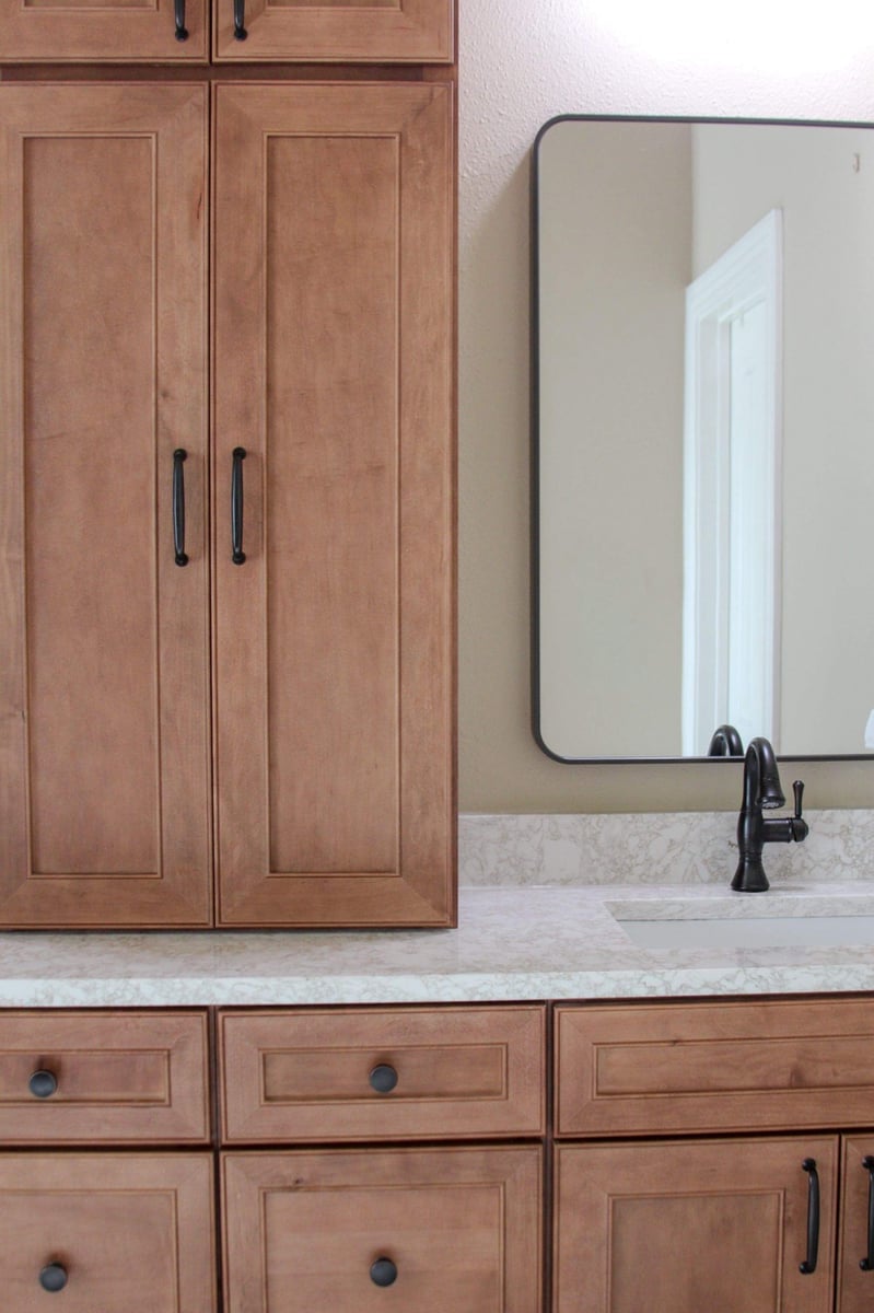 Close-up of stained maple cabinetry, quartz top, and black-framed mirror