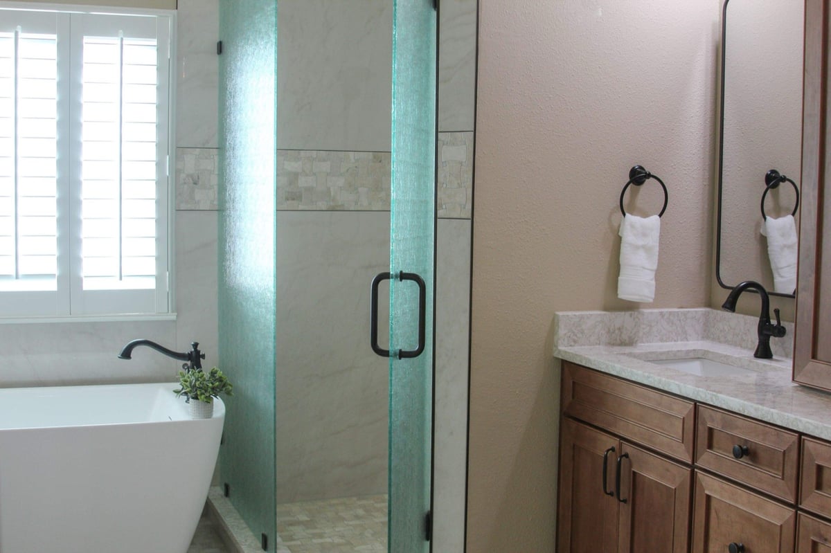 Glass shower with marble accent band, maple vanity, and bronze fixtures