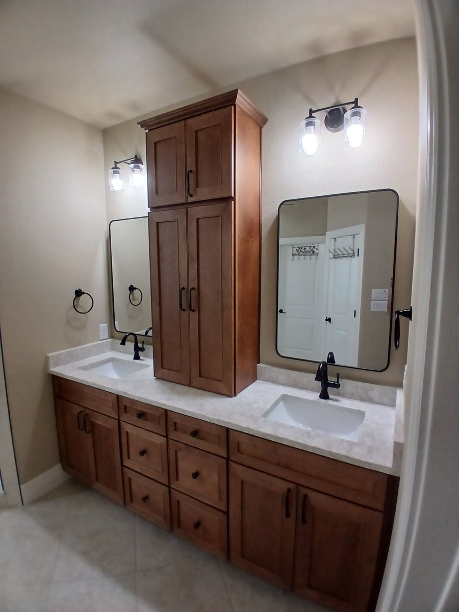 Angled view of maple double vanity with tower cabinet and two framed mirrors