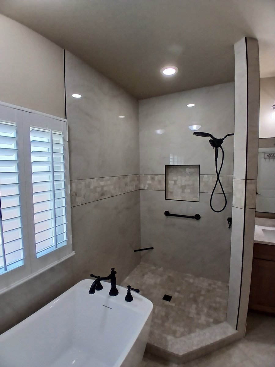 Marble walk-in shower with handheld sprayer, niche, and grab bar by the tub