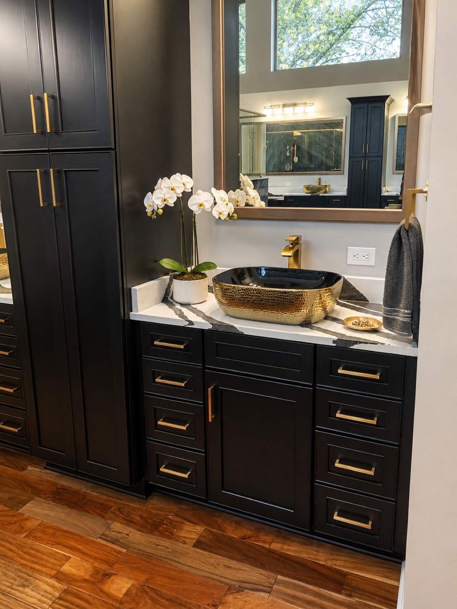Black cabinetry vanity with gold vessel sink and white orchid accent