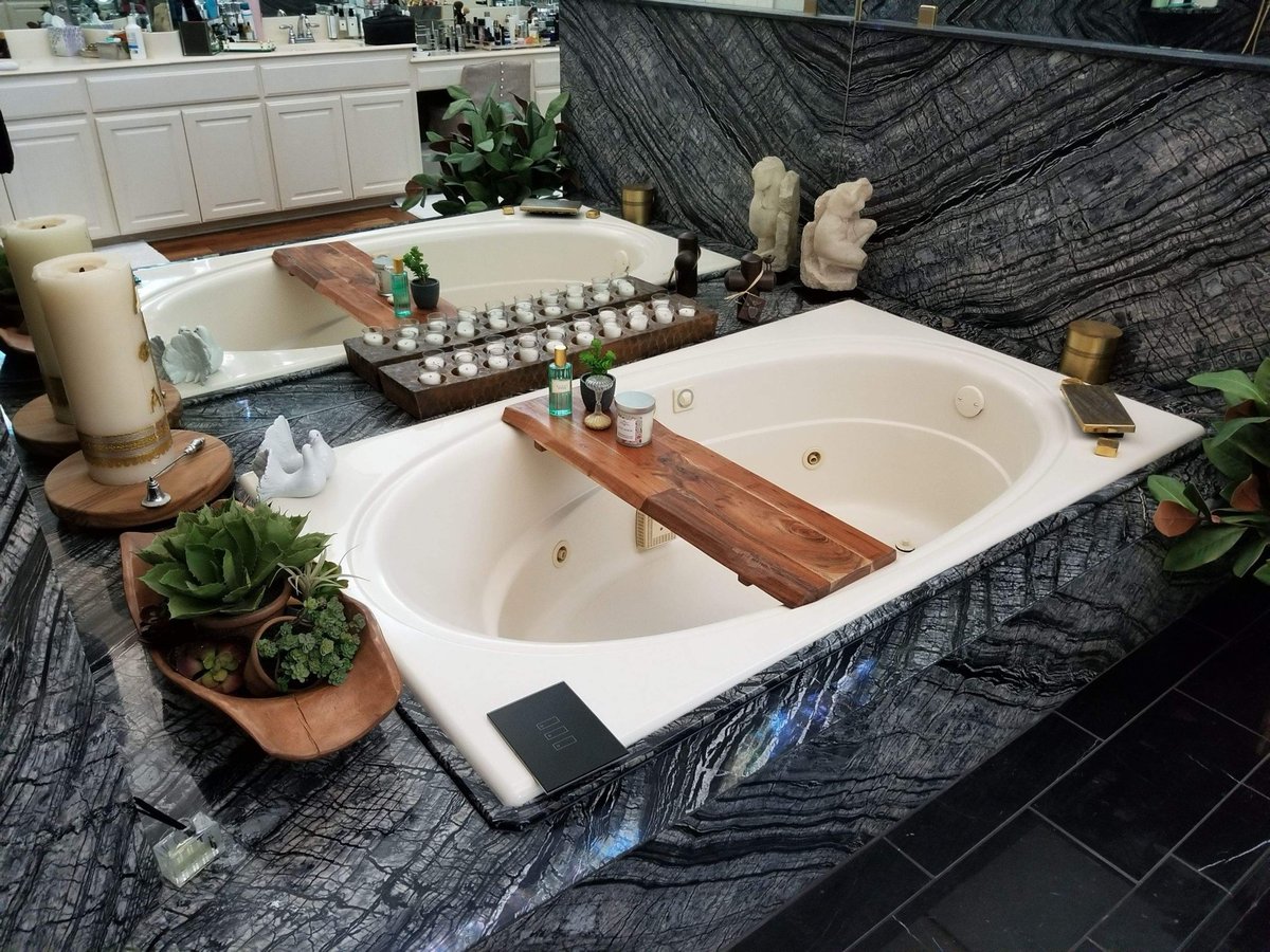 Oval soaking tub with wood bath caddy against black marble surround
