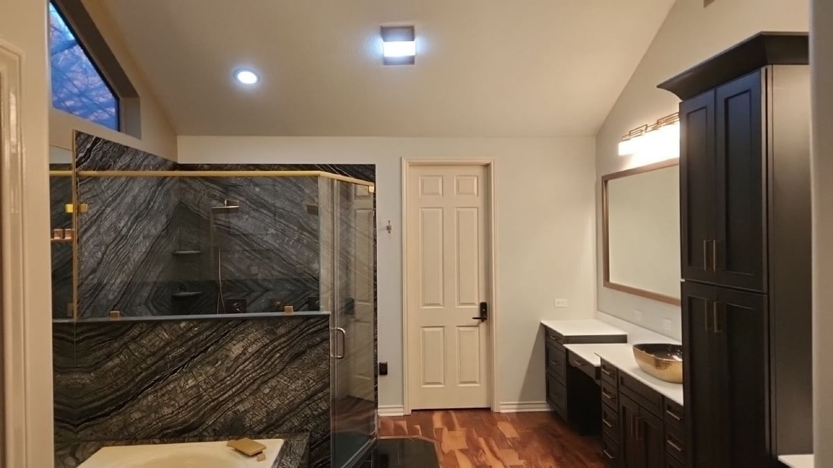 Wide master bath with stone shower, dark cabinetry, and gold vessel sink