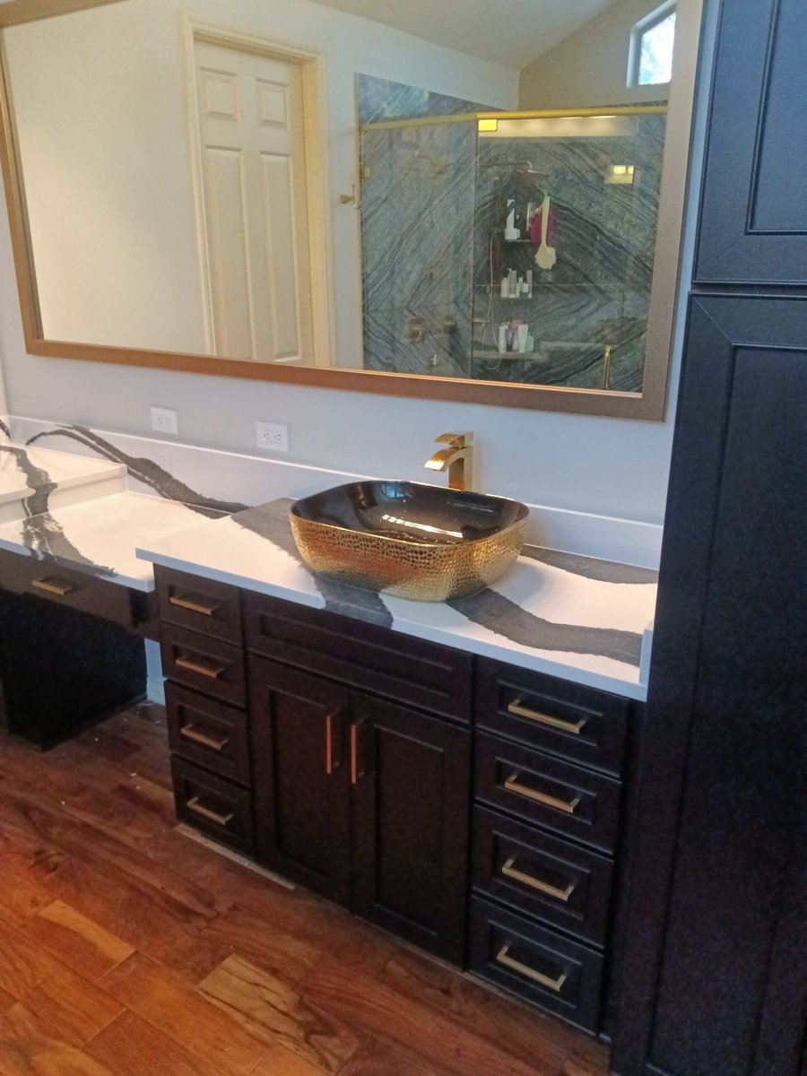 Gold vessel sink on black-and-white veined quartz over dark cabinetry