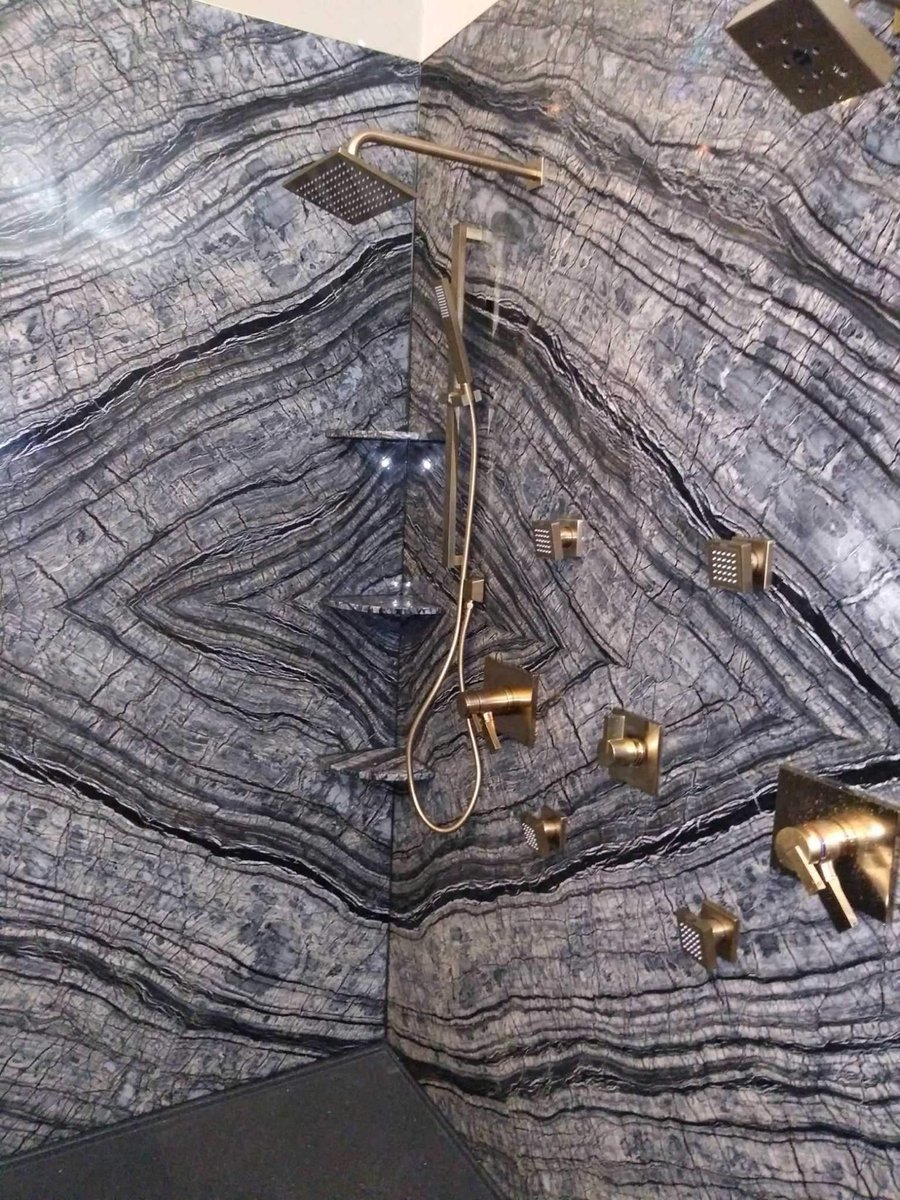 Detail of black-vein natural stone shower wall with gold body sprays