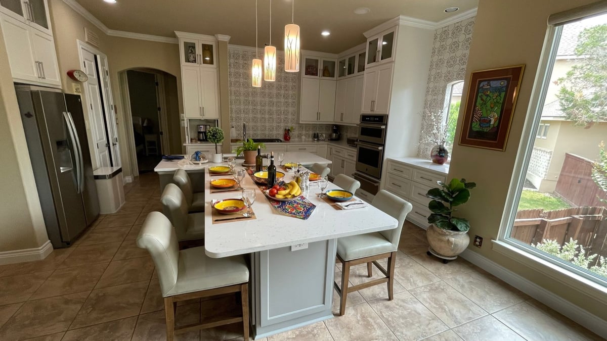 Remodeled kitchen with large white quartz island, leather barstools, and white shaker cabinets
