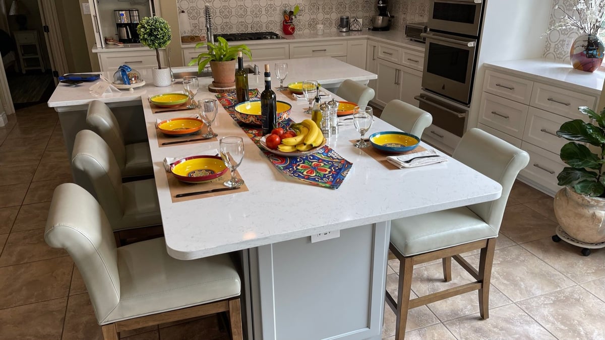 White quartz dining island set for six with green leather chairs and double wall ovens