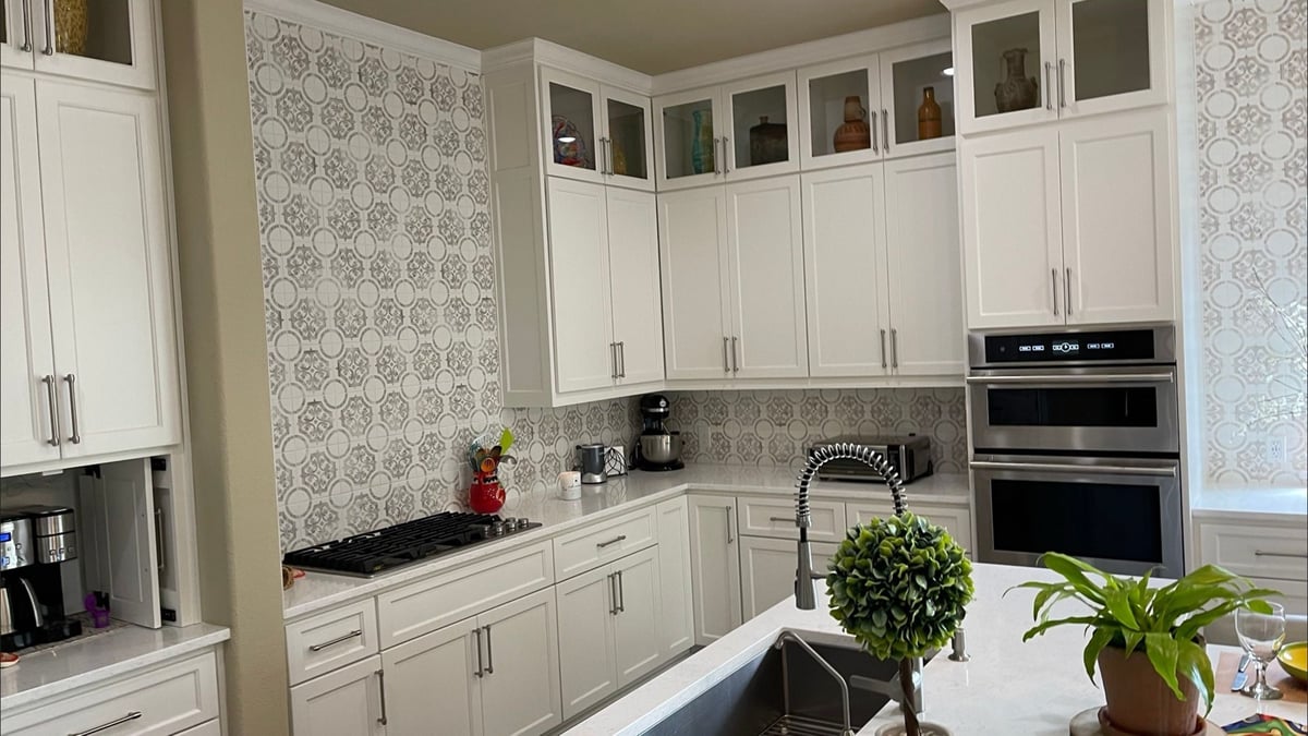 White shaker cabinets with gray patterned tile backsplash, gas cooktop, and stacked wall ovens