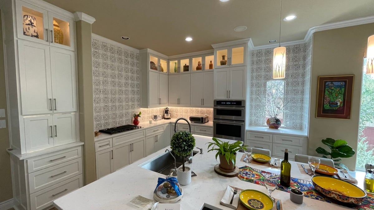White cabinet kitchen with arabesque tile backsplash, island sink, and stainless wall ovens