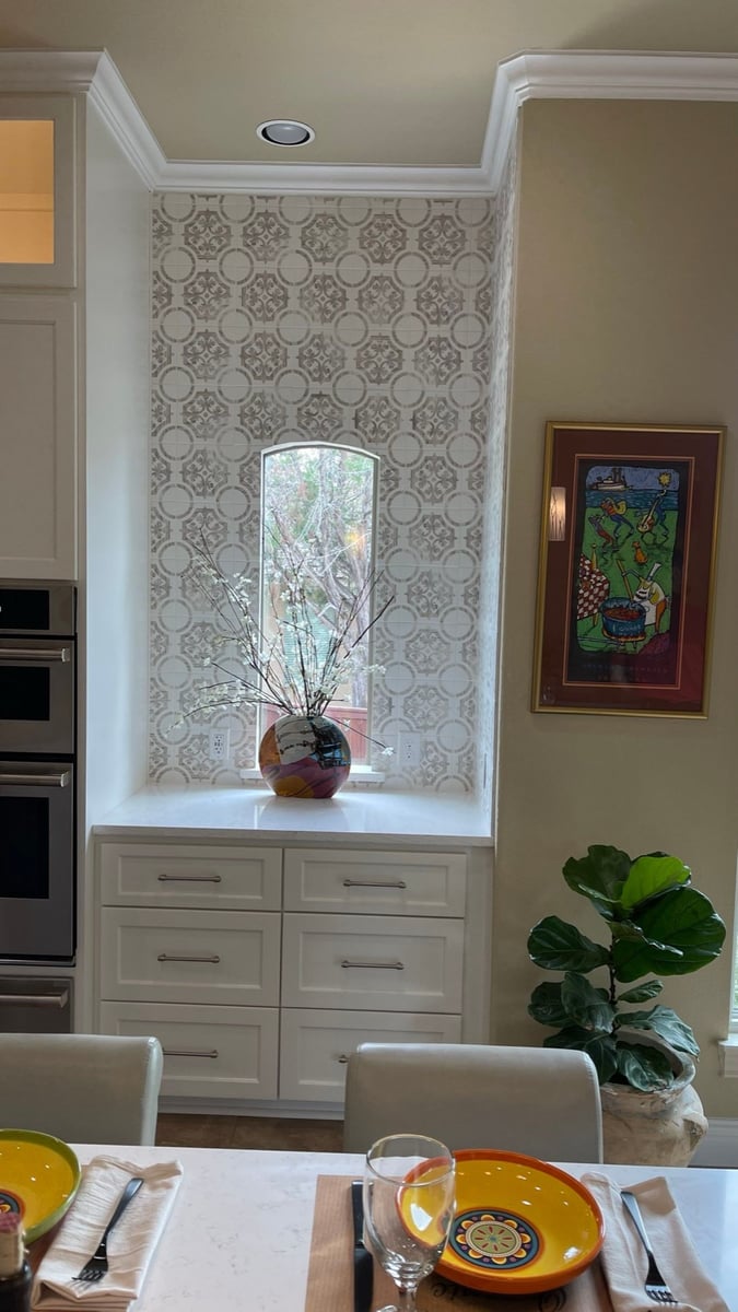 Patterned tile niche with arched window above white cabinet drawers and quartz top