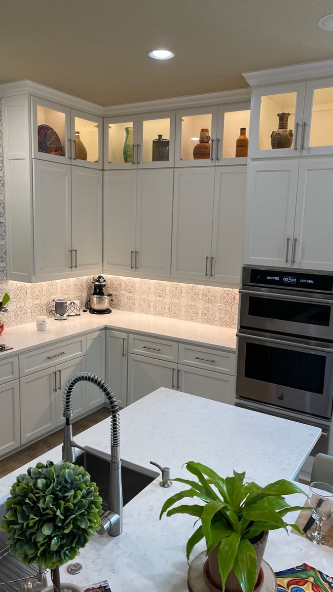 Lit glass-front cabinets displaying pottery above patterned tile and quartz countertop