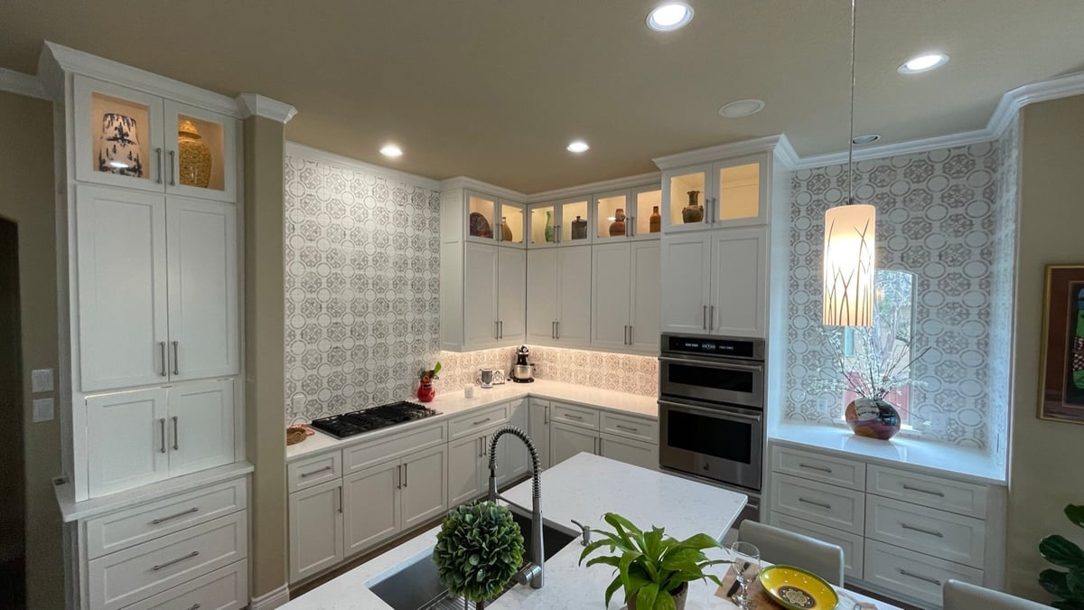 Wide view of white kitchen with patterned tile walls, island sink, and recessed lighting