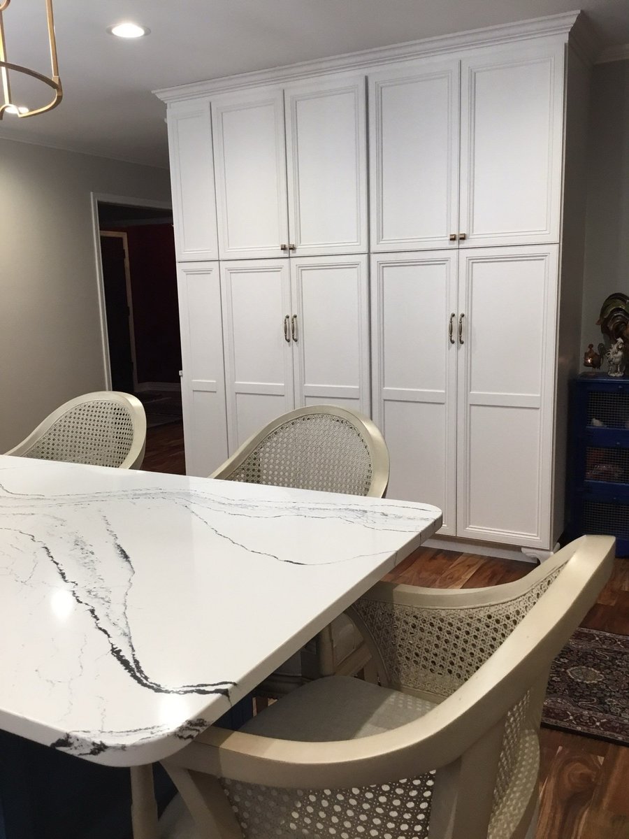 Navy cabinets and white veined quartz dining island with caned chairs