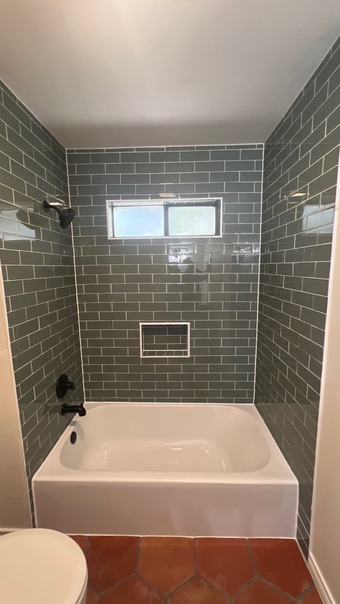Green subway tile tub surround with recessed niche, black trim, and frosted privacy window