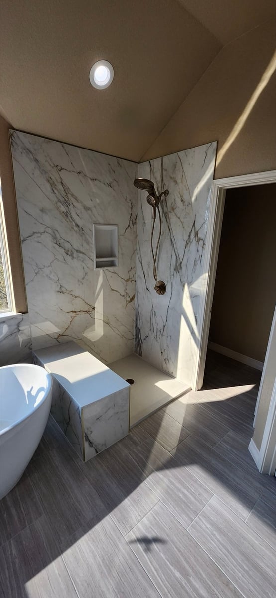 Open marble walk-in shower with built-in bench, niche, and aged brass fixtures