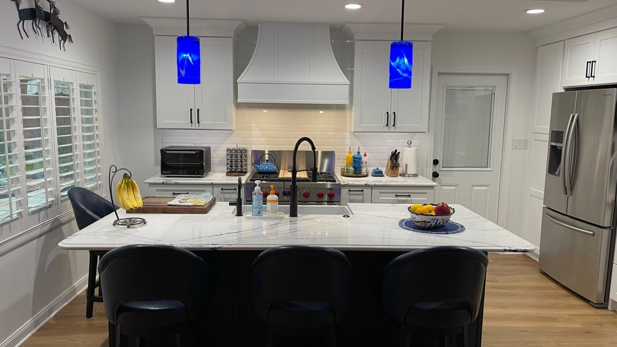 Kitchen with white cabinets, marble island, blue pendants, and pro gas range