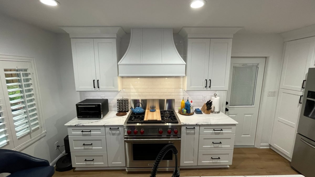Stainless pro range under white wood hood with subway backsplash and white cabinets