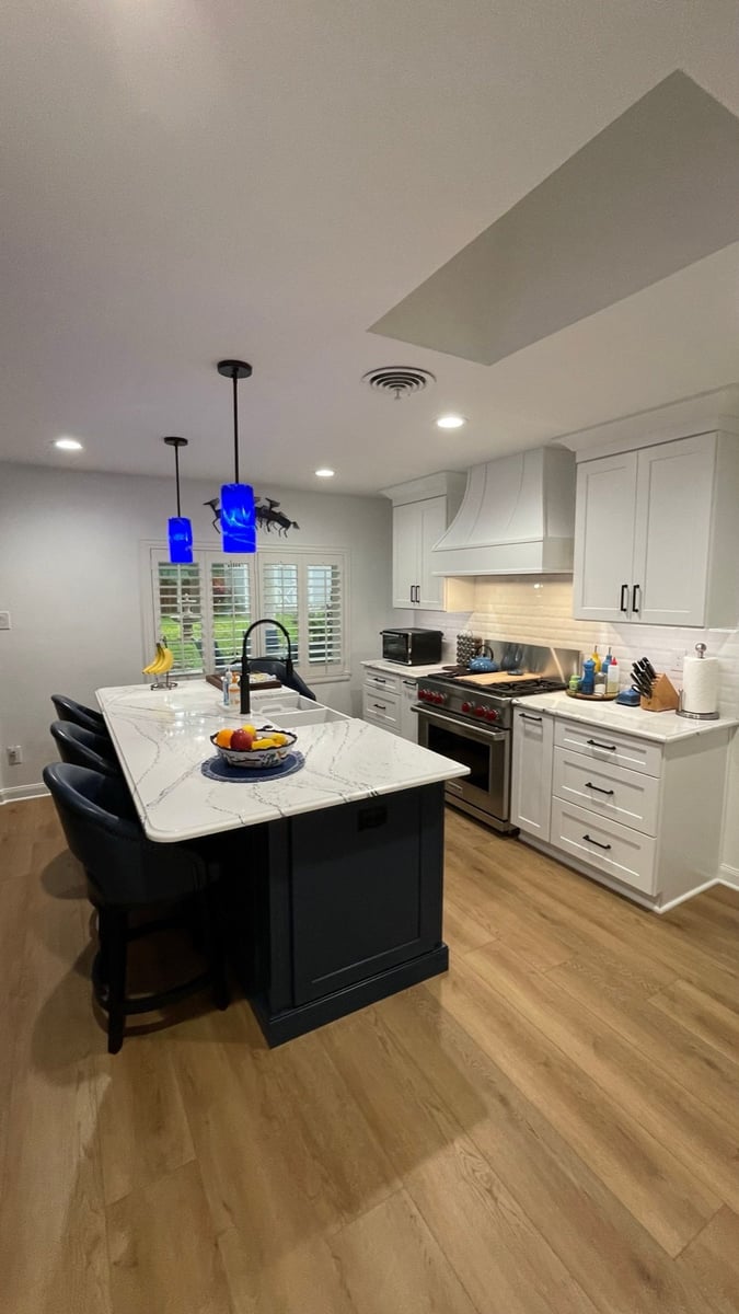 Kitchen with navy island, marble top, blue pendants, and stainless range