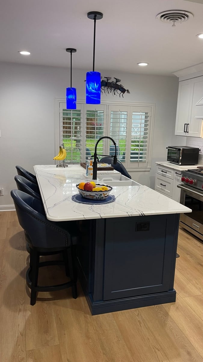 Navy kitchen island with marble counter, black faucet, and leather counter stools