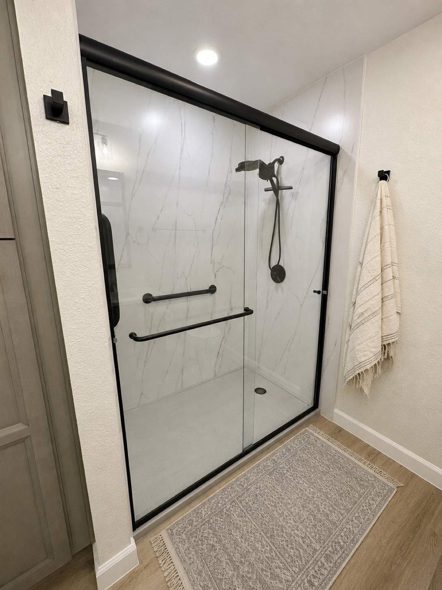 Walk-in shower with white marble walls, black-framed glass door, and black fixtures