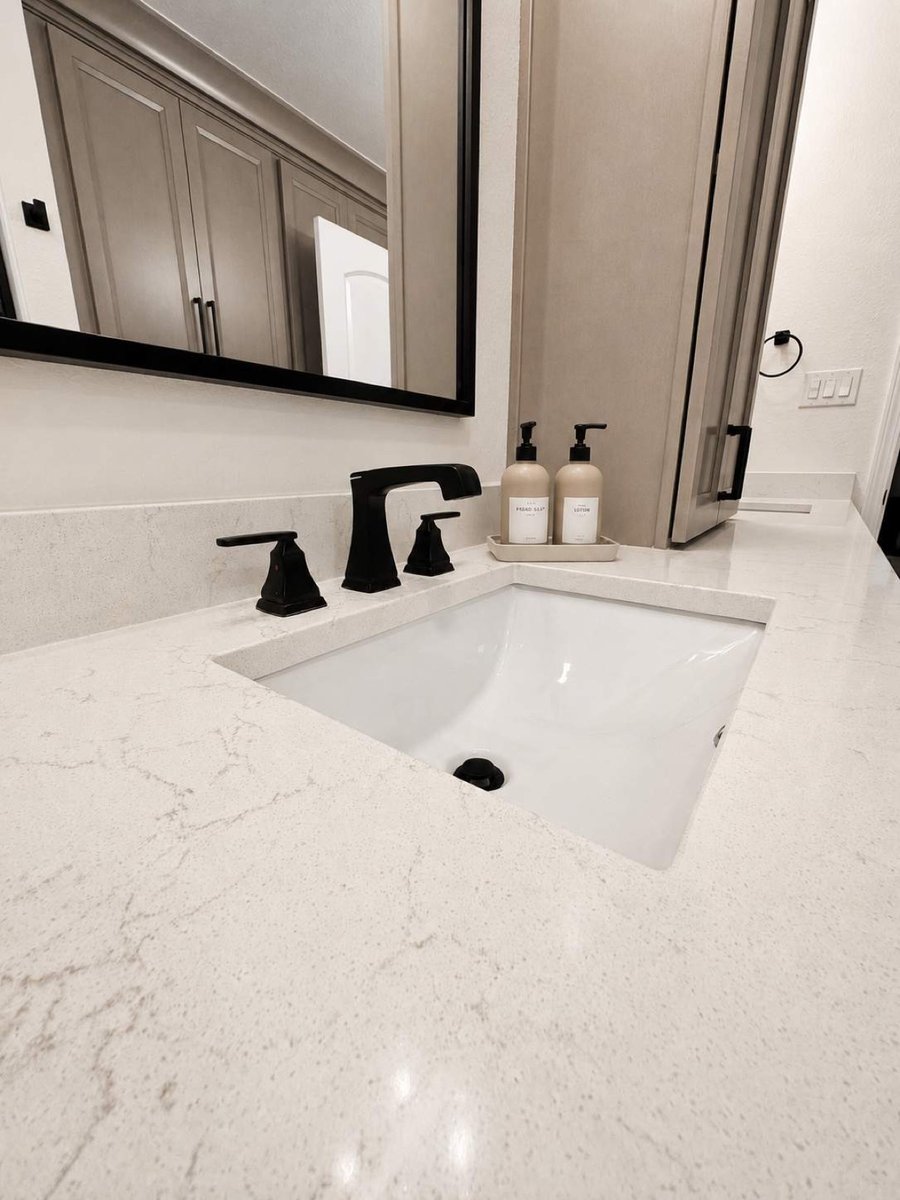 Close-up of white quartz vanity with undermount sink and black widespread faucet