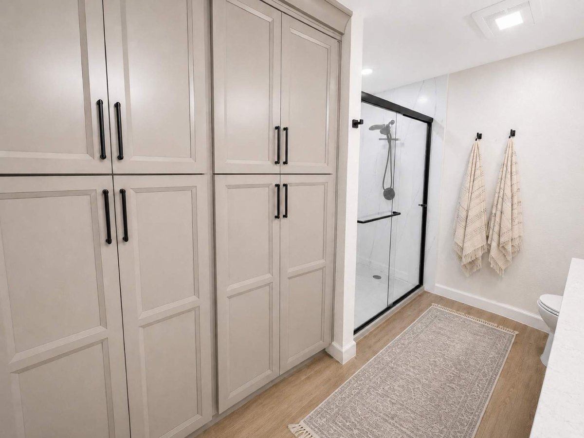Tall greige linen cabinets beside marble walk-in shower with hanging towels