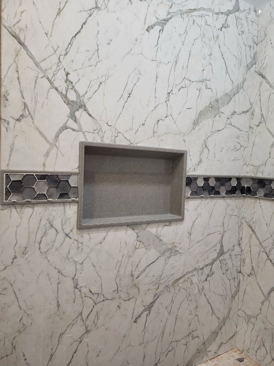 Recessed shower niche in white marble tile with gray hexagon mosaic accent band