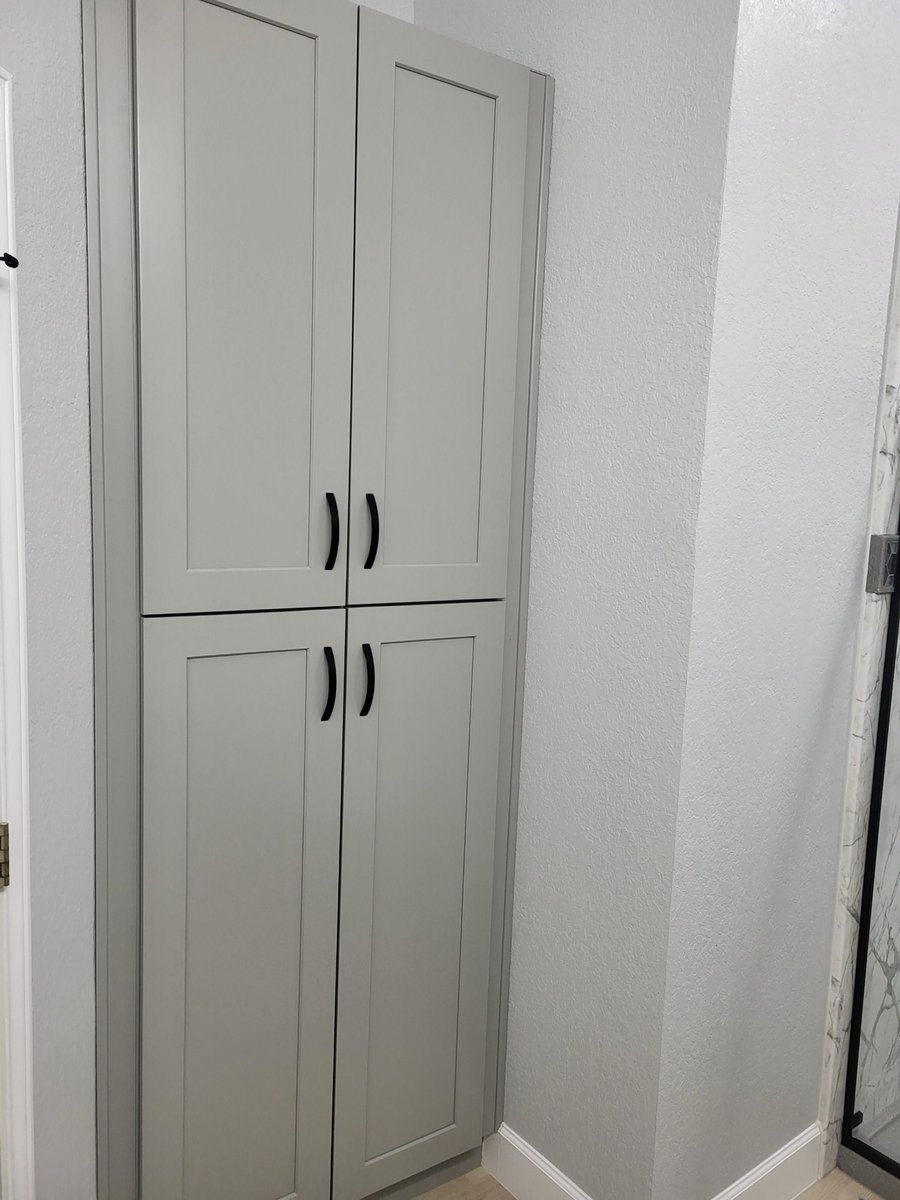 Tall gray shaker linen cabinet built into corner beside marble shower wall