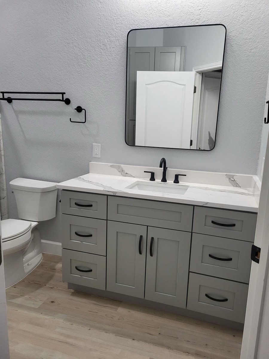 Gray vanity with marble quartz top, black framed mirror, and white toilet on wood-look floor