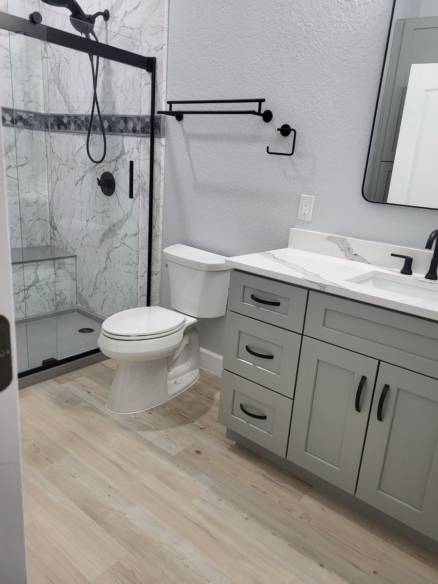Walk-in marble shower with black fixtures next to gray vanity and toilet