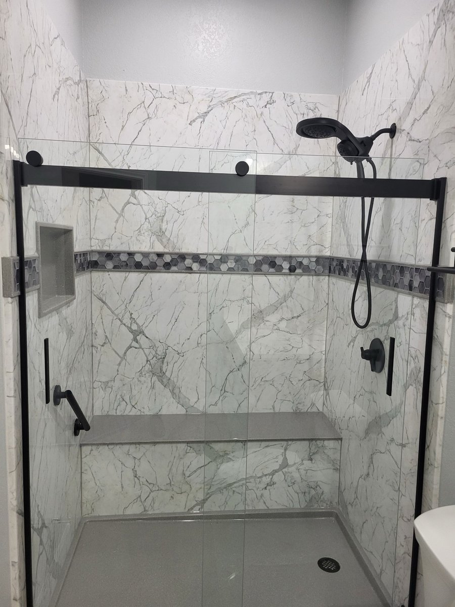 White marble walk-in shower with built-in bench, black hardware, and hexagon accent band